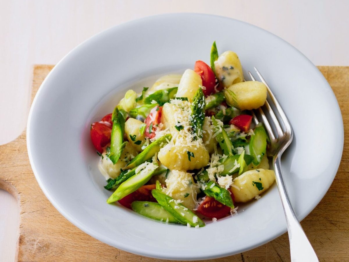 Ein weißer Telle mit Gnocchi mit grünem Spargel, Tomaten und Käse