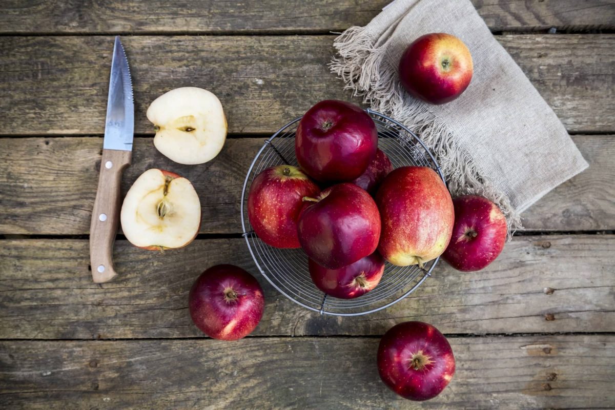 Äpfel mit Messer, Tuch und Obstkorb auf Holz-Untergrund