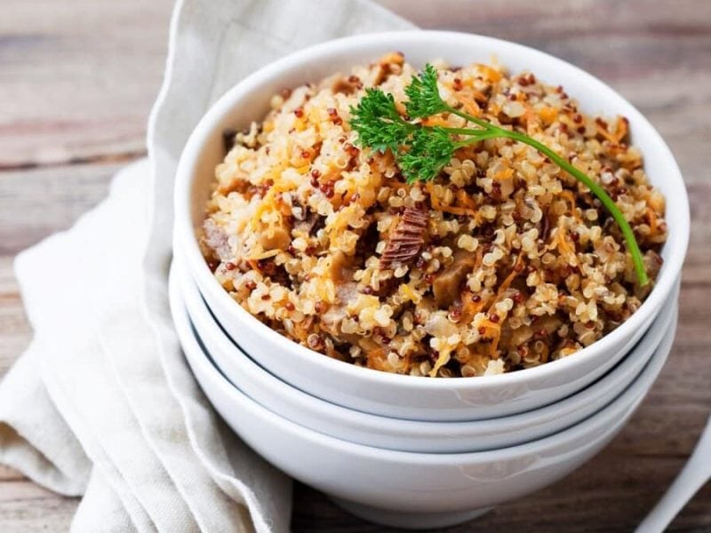 Eine weiße Schüssel steht auf einem Holztisch. In der Schüssel ist ein Quinoa-Risotto mit Champignons. / Foto: iStock/laperla_foto