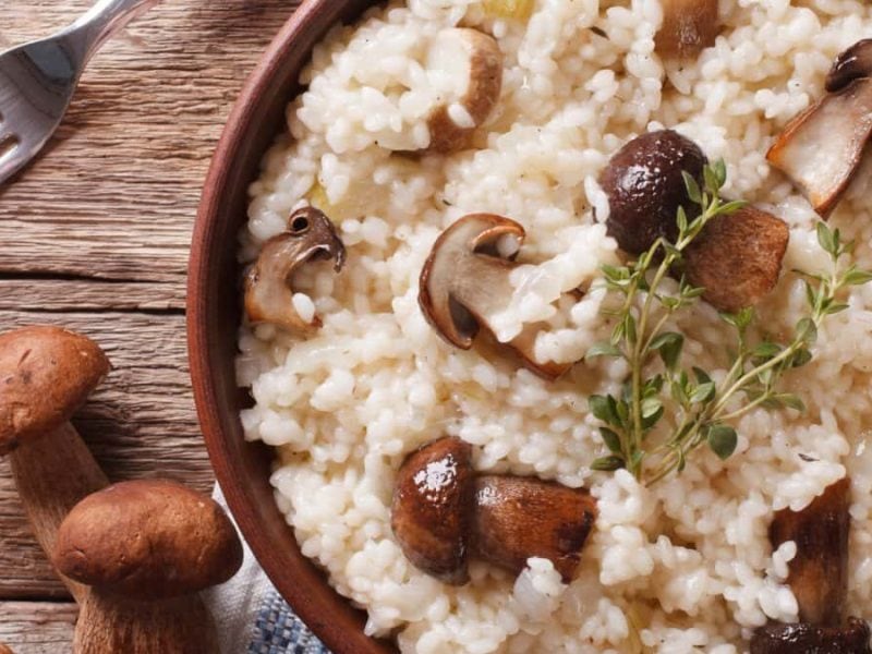 Auf einem Holztisch steht eine Topf mit einem Steinpilz-Risotto.