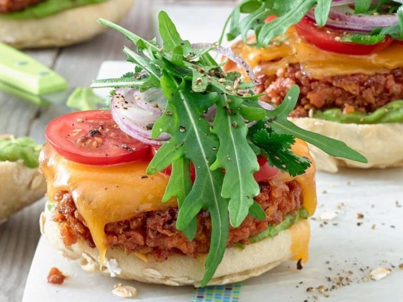 Auf einem weißen Brett liegen drei vegetarische Soja Burger mit Broetchen und Avocado. Nicht alle sind gleich groß.