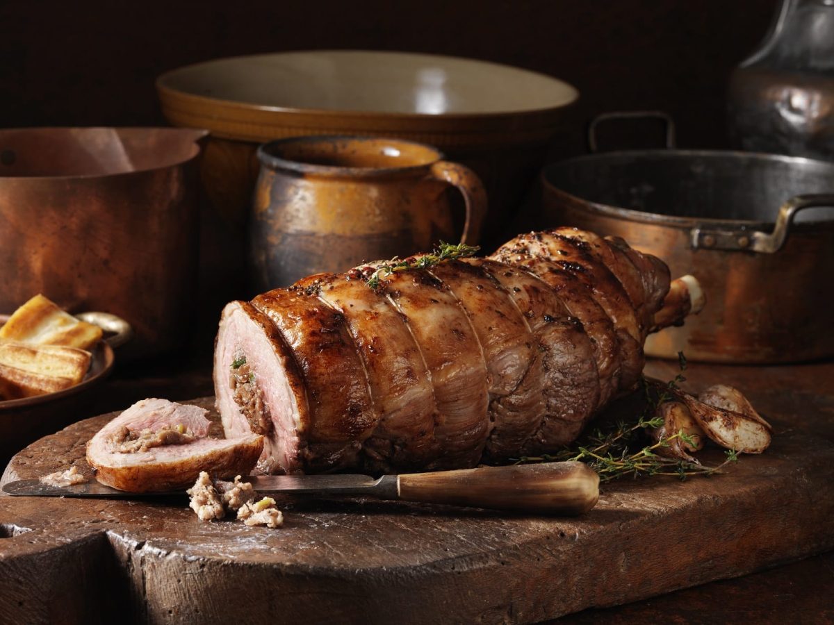 Braten auf Holzbrett mit Töpfen im Hintergrund