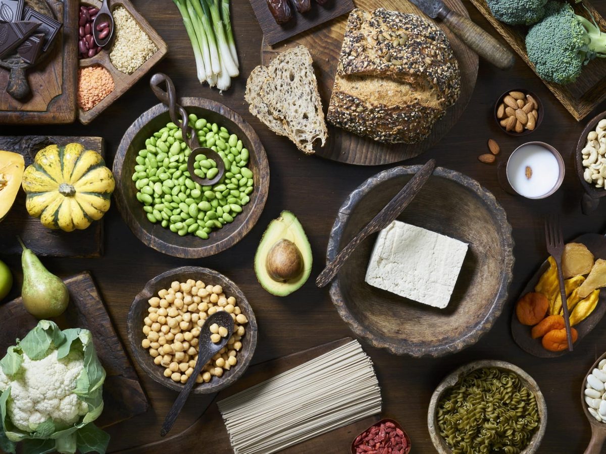 eine Auswahl an ballaststoffreichen Lebensmittel wie Brot, Kichererbsen, Blumenkohl, Brokkoli, Bohnen und mehr in der Draufsicht.