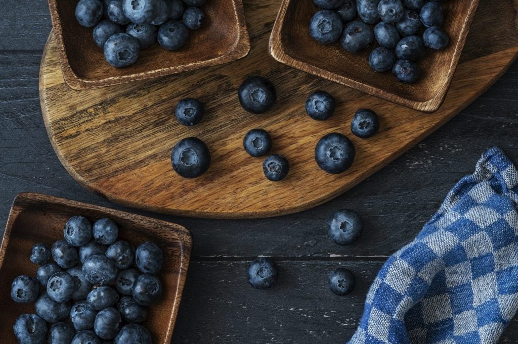Ballaststoffreiche Lebensmittel: Holzschalen mit Blaubeeren auf dunklem Holztisch