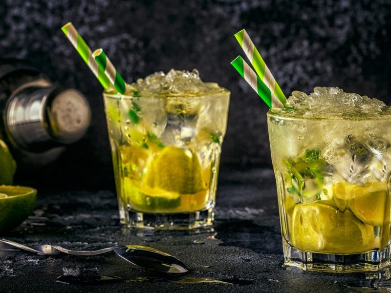 Caipirinha-Bowle in zwei Gläsern mit Strohalmen, Eis und Limetten.