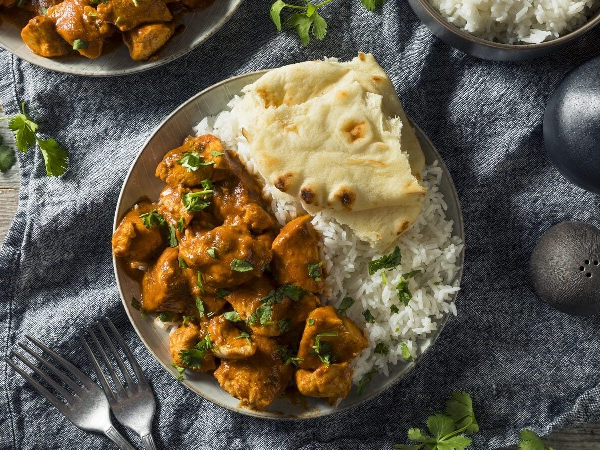 Schale mit Chicken Tikka und Nuss-Pilaw mit Naan-Brot auf einer Tischdecke von oben