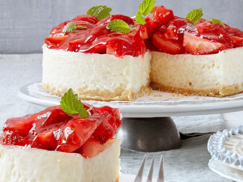 Aufgeschnittene Erdbeertorte mit Milchreis auf einem hellen Tisch mit einer grauen Tischdecke vor einem grauen Hintergrund.