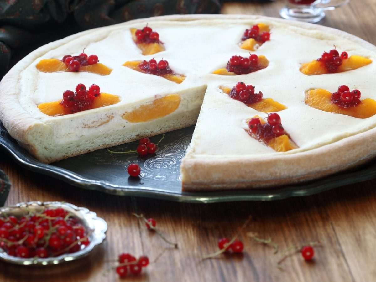 Tarte mit griechischem Joghurt und Früchten auf schwarzem Teller, daneben Johannisbeeren