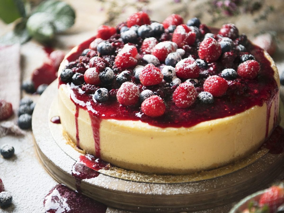 Himbeer-Schmand-Torte ohne Backen mit Himbeeren, Blaubeeren und roter Soße dekoriert.