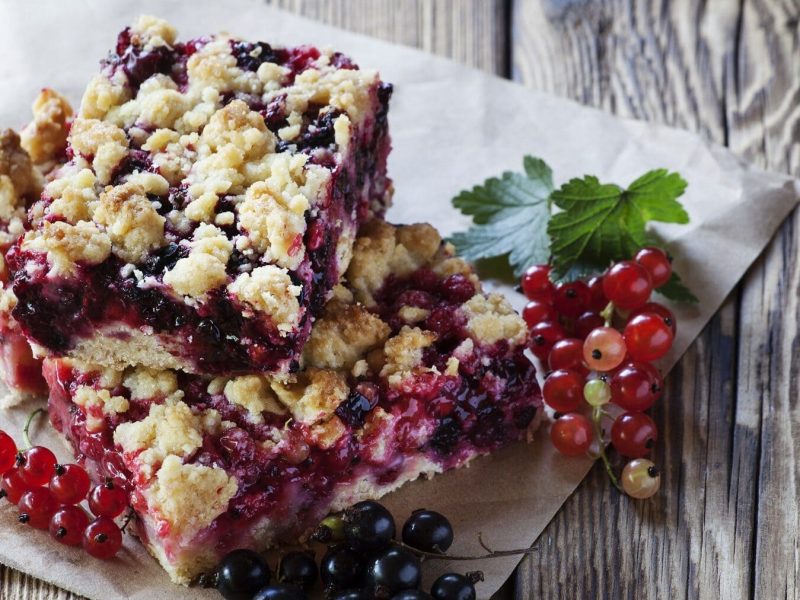 Streuselkuchen mit roten und schwarzen Johannisbeeren auf einem Stück Papper auf einem unbehandelten Holztisch.