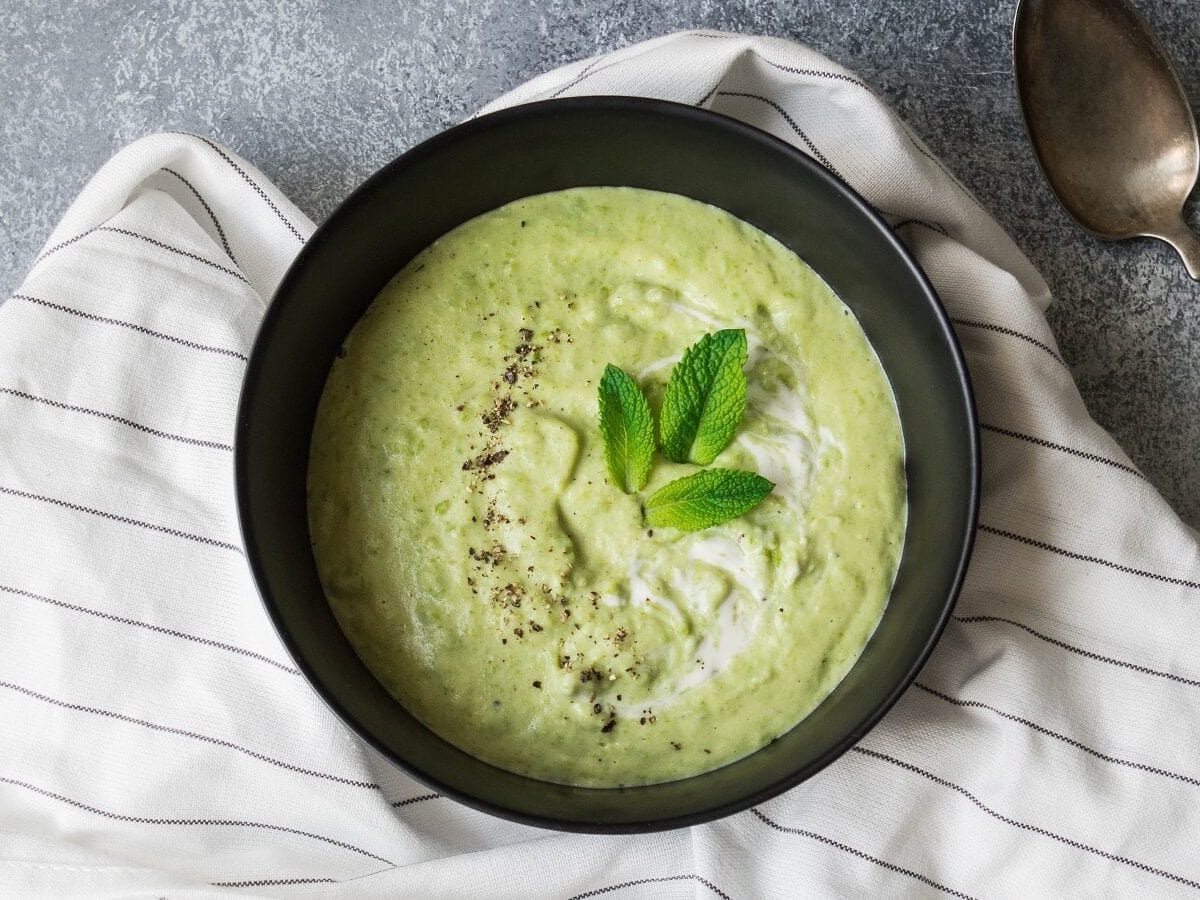 Kalte Gurkensuppe mit Minzblättern garniert und in einer schwarzen Schüssel serviert, von oben auf grauem Hintergrund