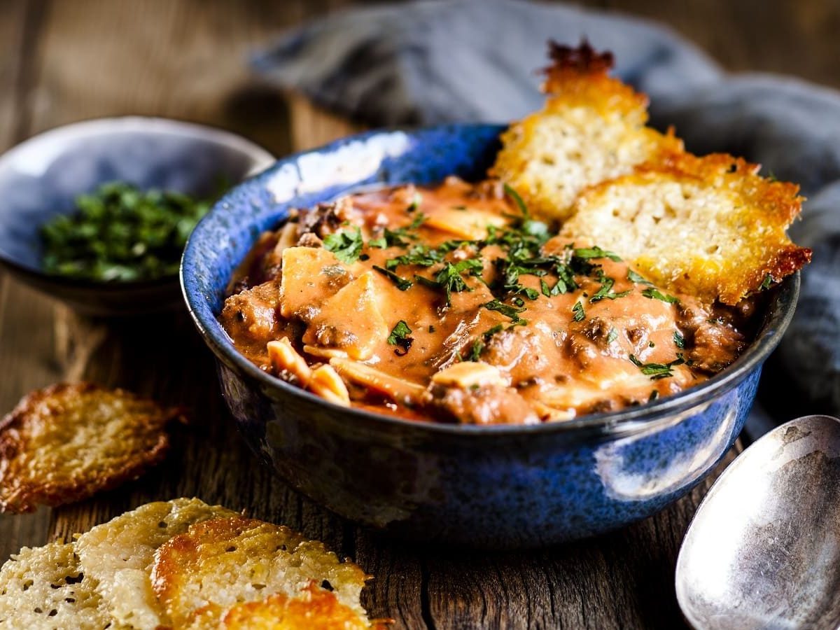 Eine Schüssel mit Lasagne-Suppe, garniert mit Basilikum und Parmesan Crisps auf einem Holztisch