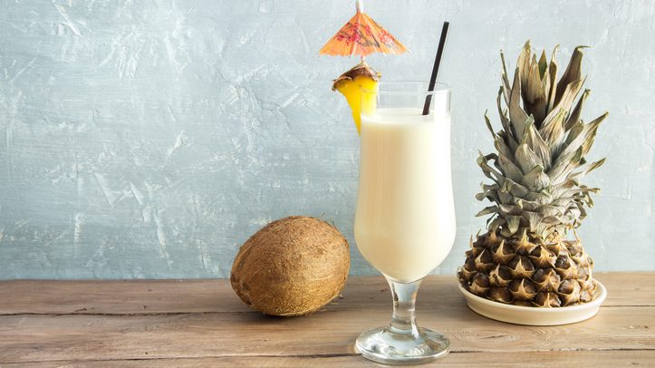 Ananas-Cocktail im Glas mit Schirmchen, daneben abgeschnittene Ananas und Kokosnuss