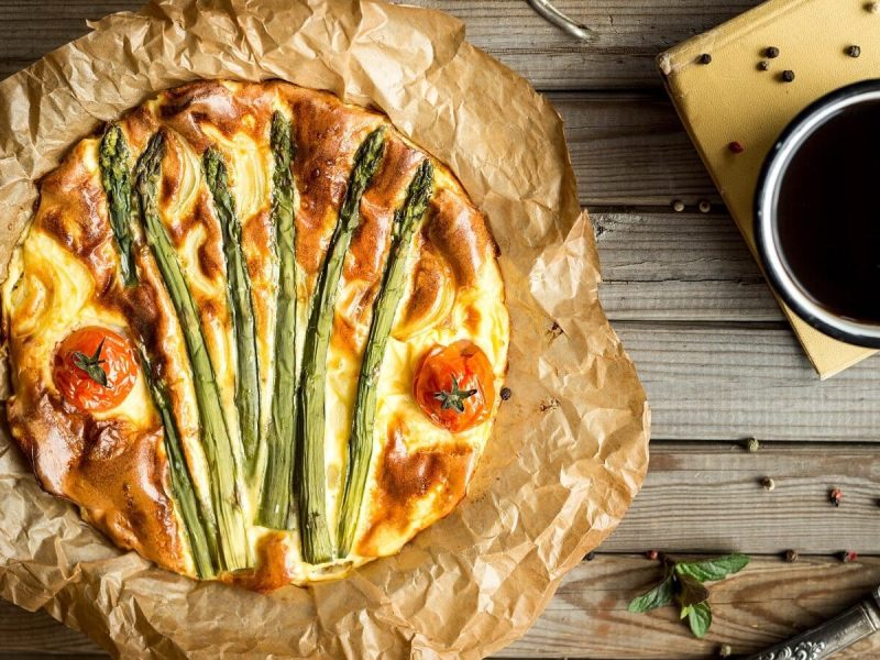 Eine frischgebackene Spargelquiche mit Kirschtomaten von oben auf Holzhintergrund