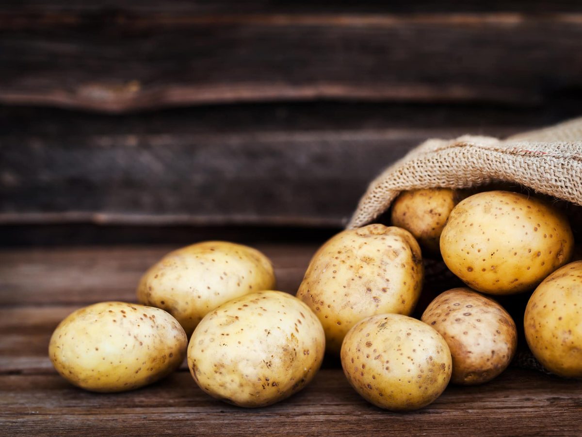 Lebensmittel, die kein Licht vertragen: ein umgekippter Sack Kartoffeln vor einem Holzhintergrund