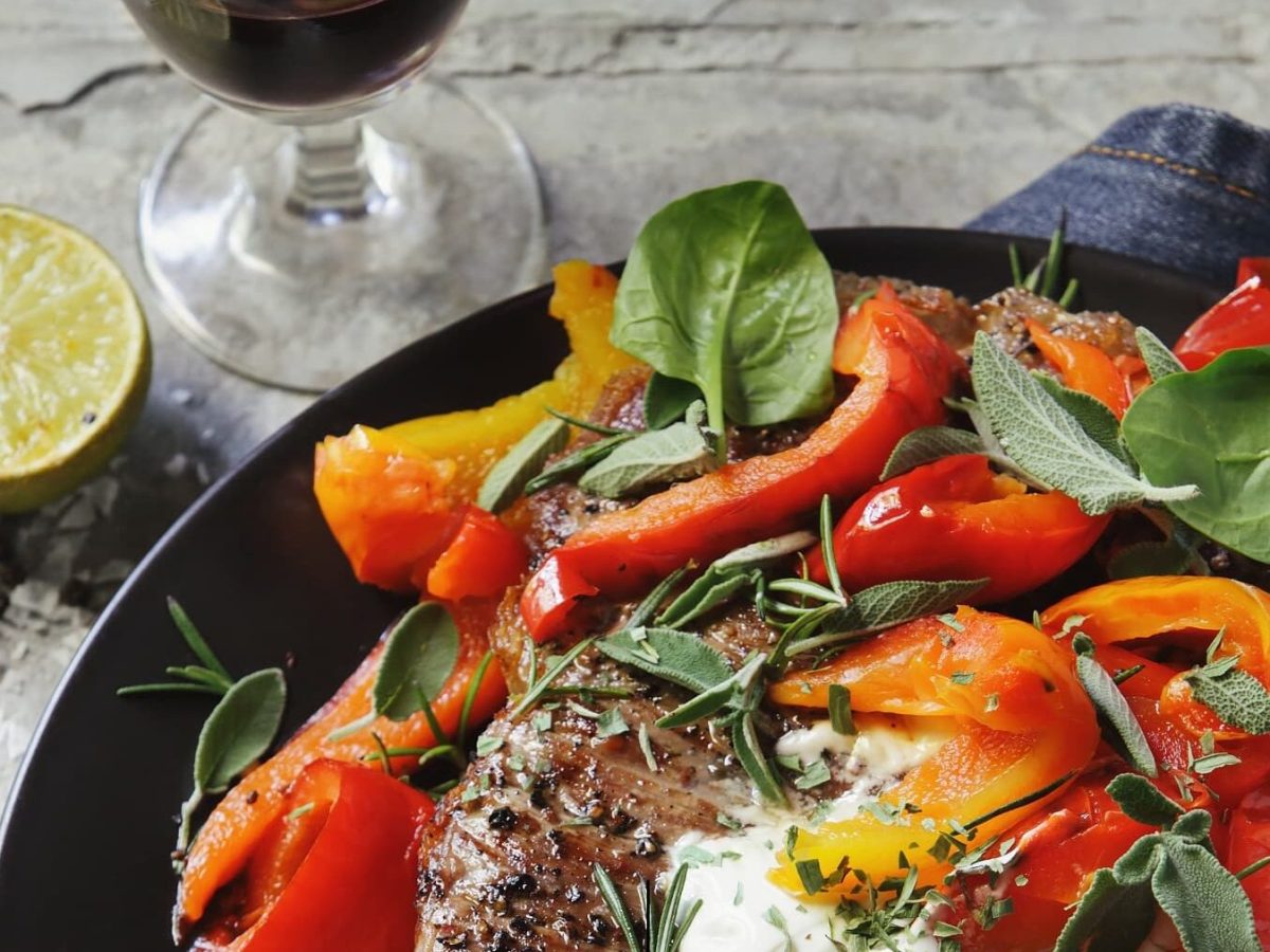 Schnelles Steak mit Paprika-Salat auf schwarzem Teller mit Steinhintergrund und einem Glas