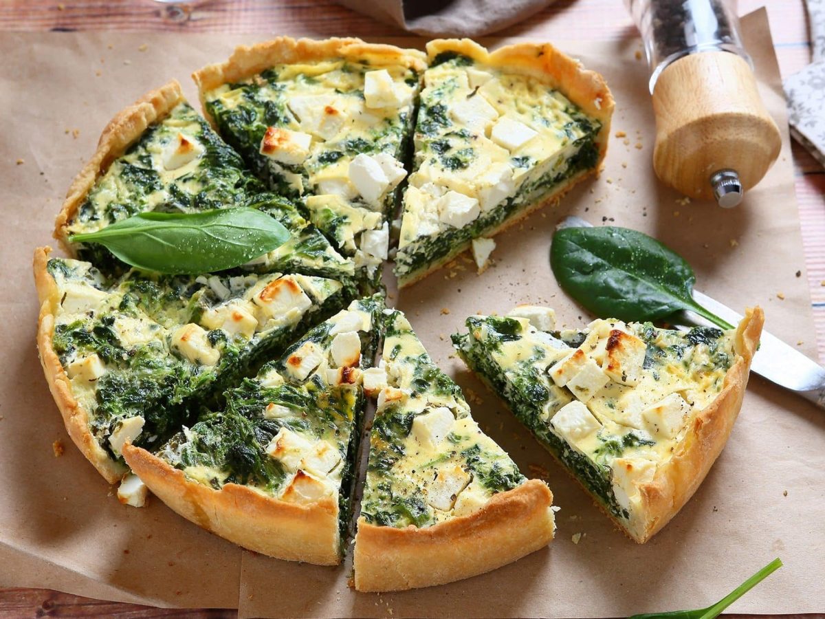 Spinat-Quiche mit Ziegenkäse und Rosinen auf Backpapier, daneben ein umgekippter Pfefferstreuer und ein Messer.