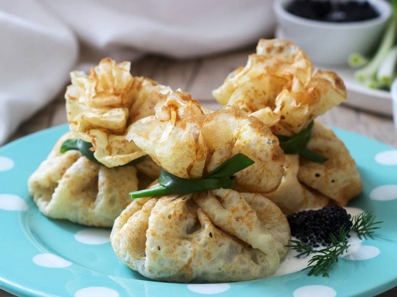 Gefüllte Pfannkuchen mit Spinat und Frischkäse auf einem blauen Teller, daneben eine Schale mit Kaviar.