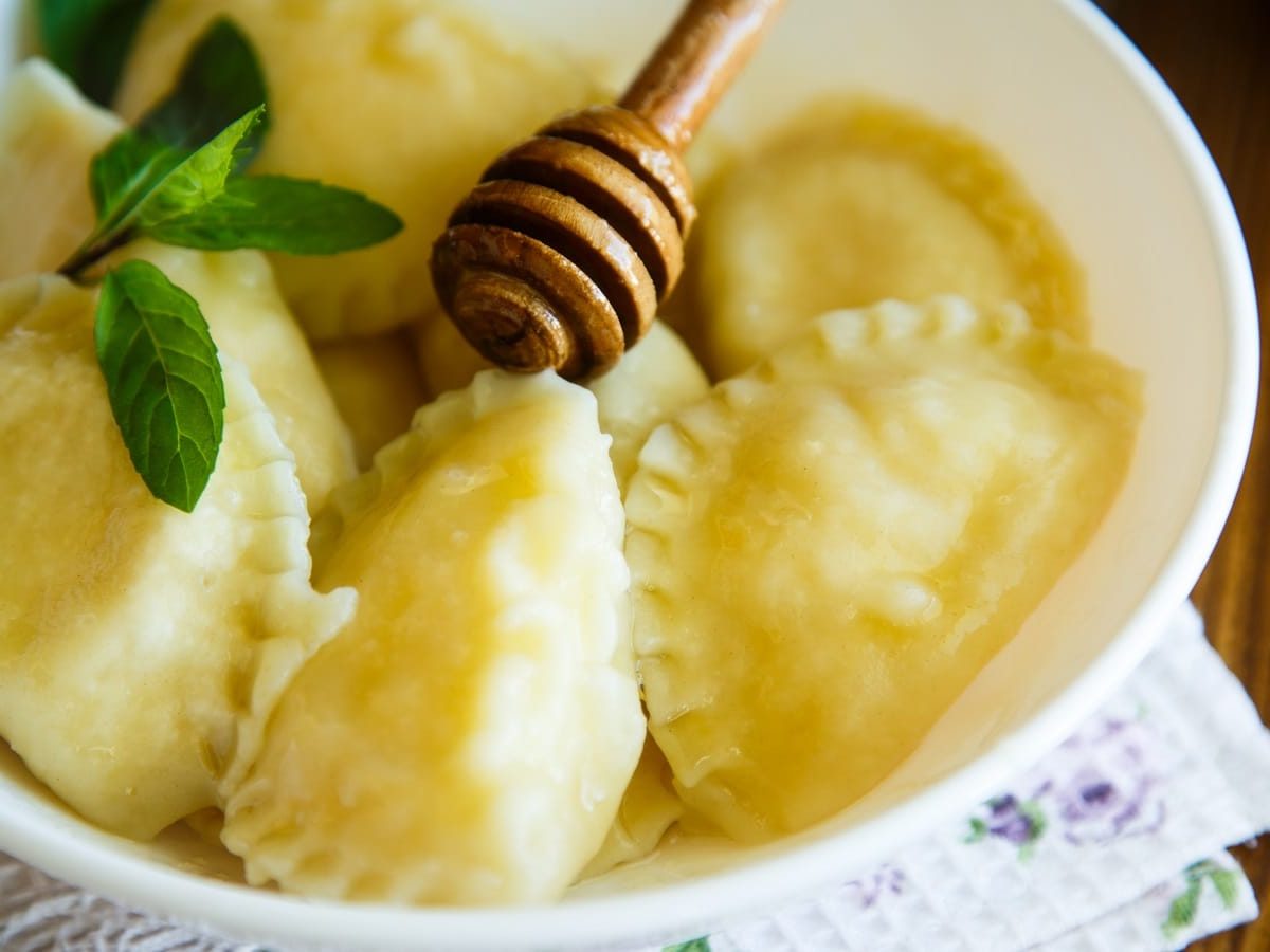 Eine weiße Schüssel gefüllt mit mehreren Ricotta Calcioni, die mit Honig glasiert und mit Minze garniert sind.