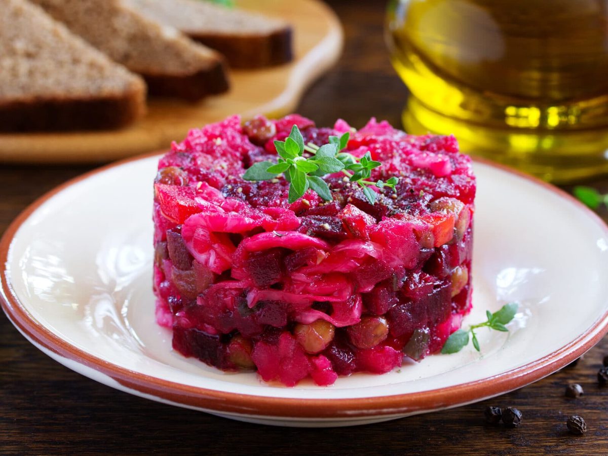 ein Teller mit Rote-Bete-Tatar, im Hintergrund unscharf eine Flasche Öl und ein paar Scheiben Toast.