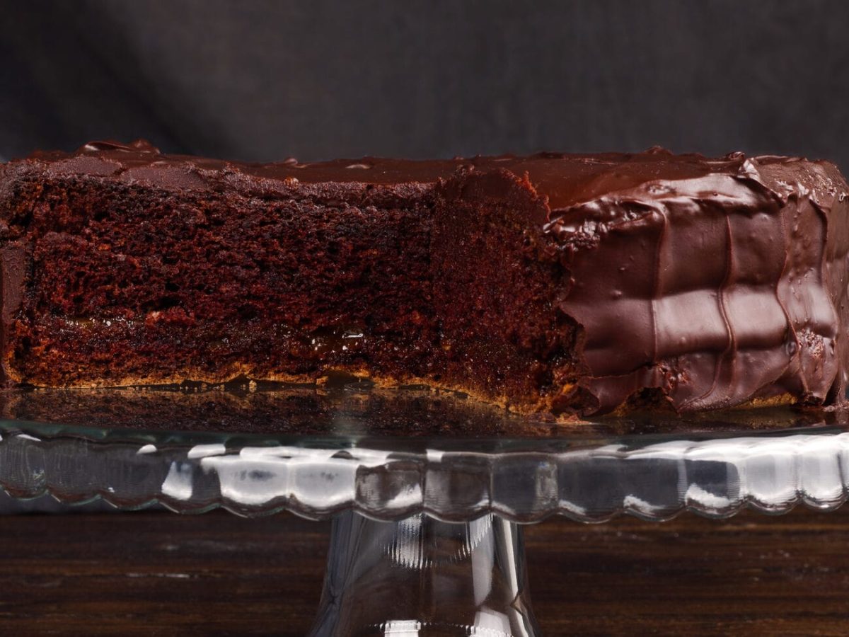 Eine angeschnittene Rum-Schokotorte auf einem Tortenständer aus Glas vor dunklem Hintergrund.