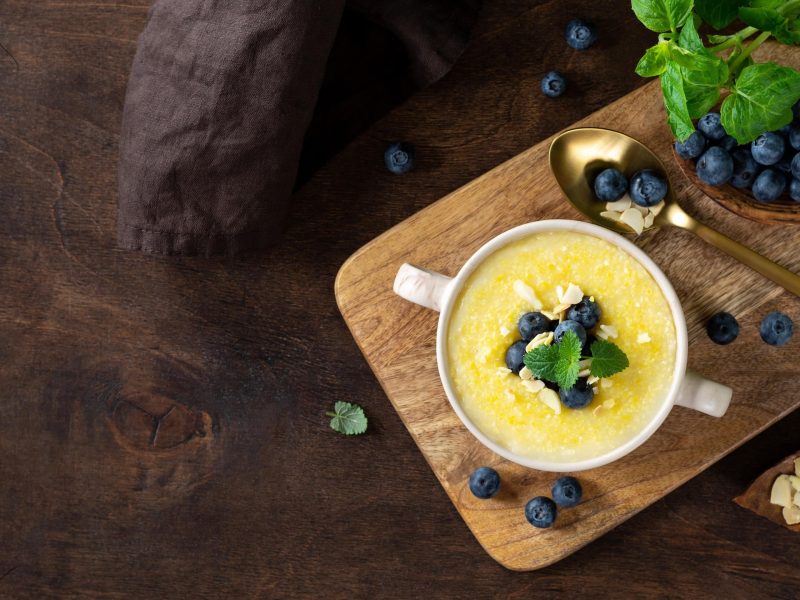 Cremige Polenta ist in einer Schüssel angerichtet mit Blaubeeren als Topping.