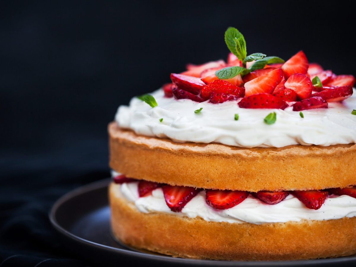 Ein Naked Cake mit Erdbeeren und Sahne auf einem Teller, dekoriert mit frischer Minze.