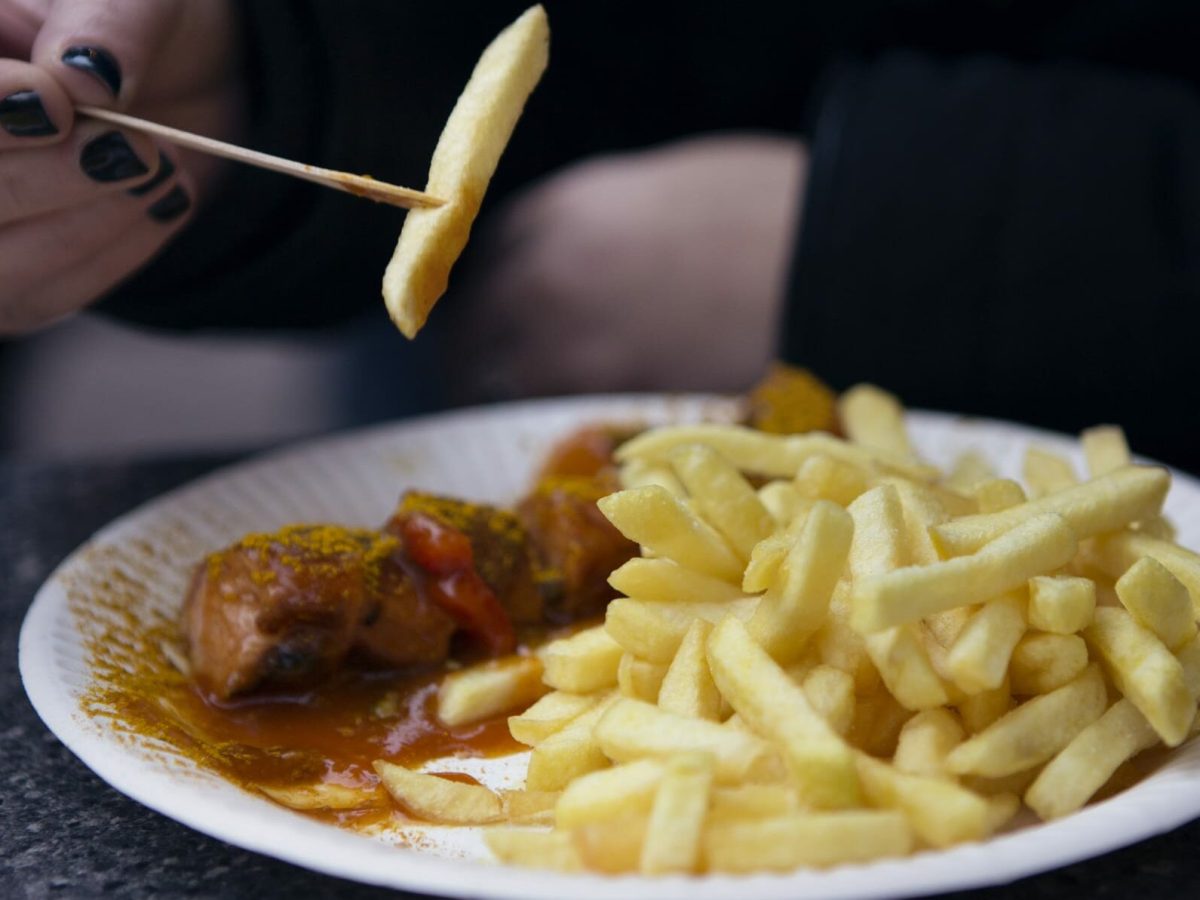 Currywurst mit Pommes, serviert auf einem weißen runden Pappteller.