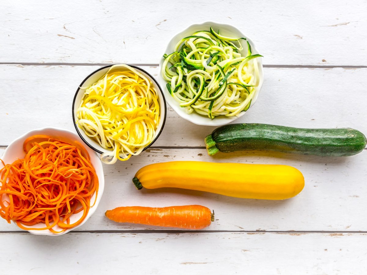 Zucchini und Möhre zu Low-Carb-Pasta verarbeitet auf weißem, hölzernem Untergrund.