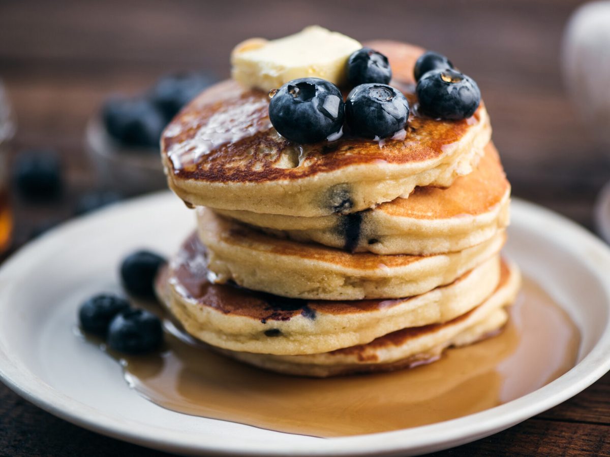 Ein Teller mit einem Stapel glutenfreier Kokos-Pancakes, dazu Blaubeeren und Sirup.