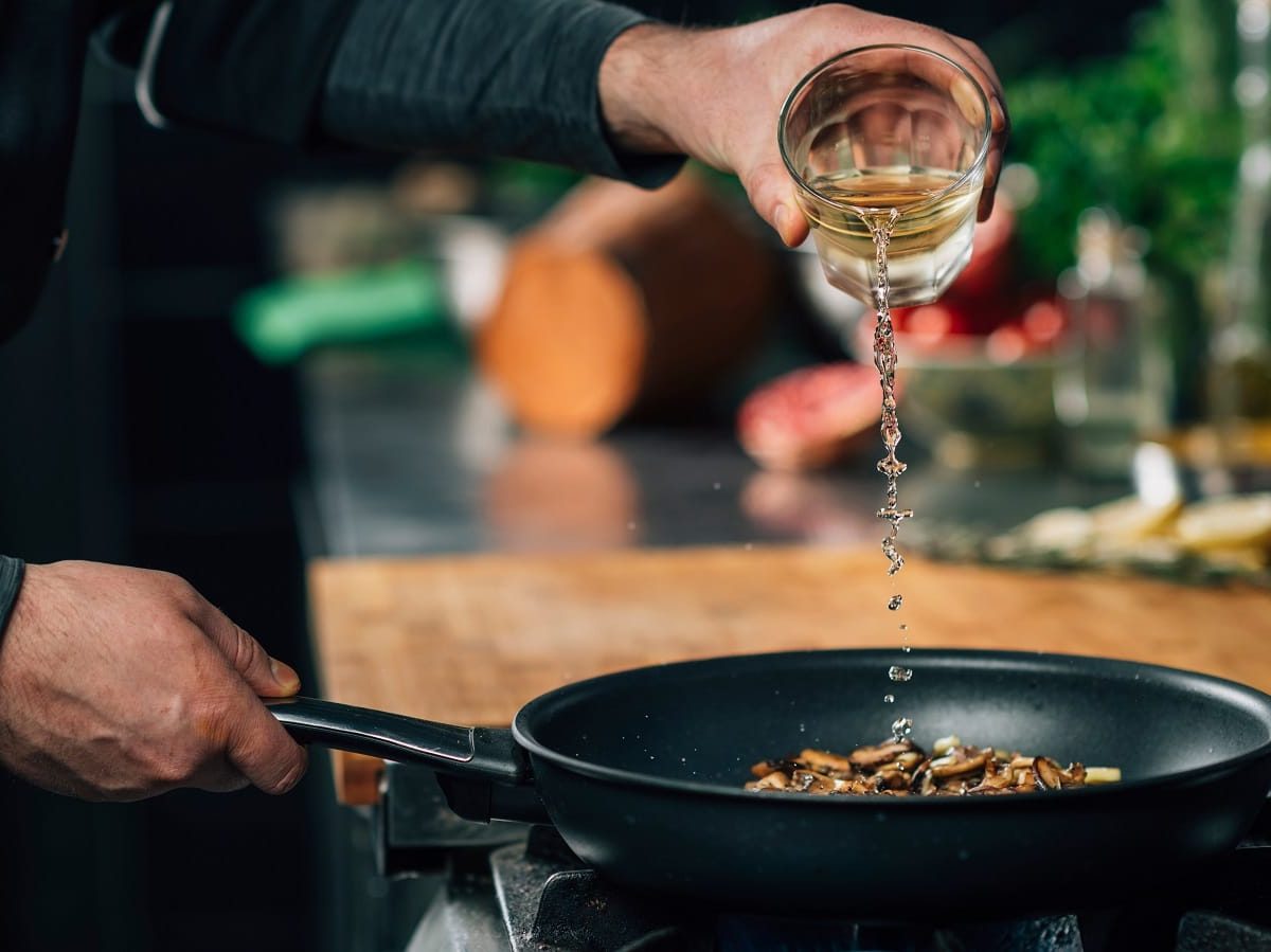 Ablöschen in der Praxis: Ein Koch gießt Weißwein in eine Pfanne mit Gemüse.