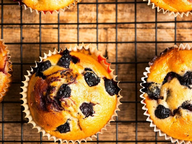 Muffins mit Aroniabeeren auf einem Rost. Das Rost steht auf einem hölzernen Untergrund.