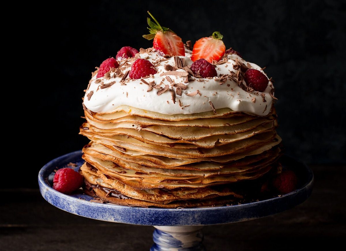 Eine Tortenplatte mit einer Pfannkuchentorte mit Blaubeercreme, dekoriert mit Schlagsahne und frischen Beeren.