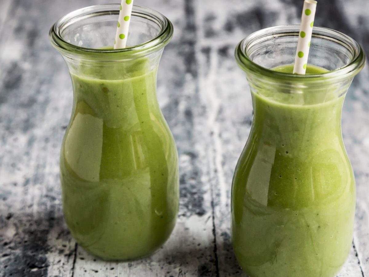 Zwei Gläser mit Smoothie mit Staudensellerie auf einem grauen hölzernen Untergrund.