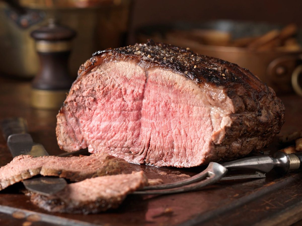 Ein Braten auf einem Holzbrett mit Tranchiermesser und -gabel.