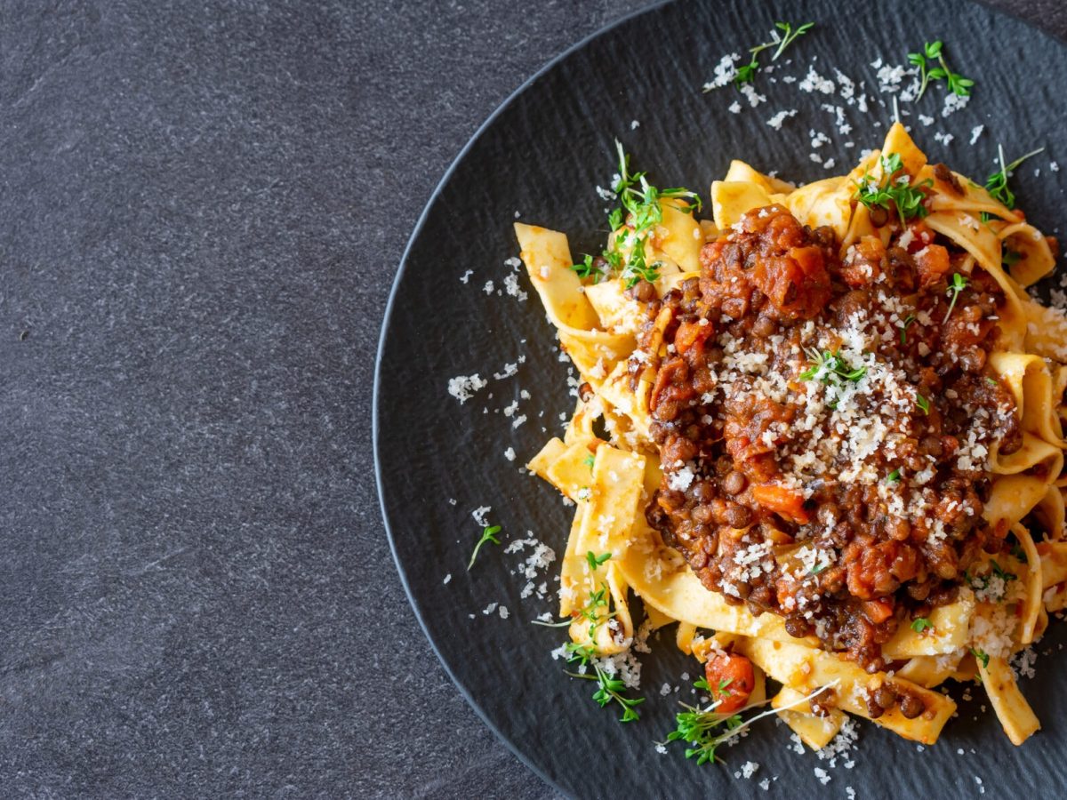 Ein Teller vegetarische Bolognese mit Linsen und Tagliatelle, bestreut mit Parmesan und Kräutern.