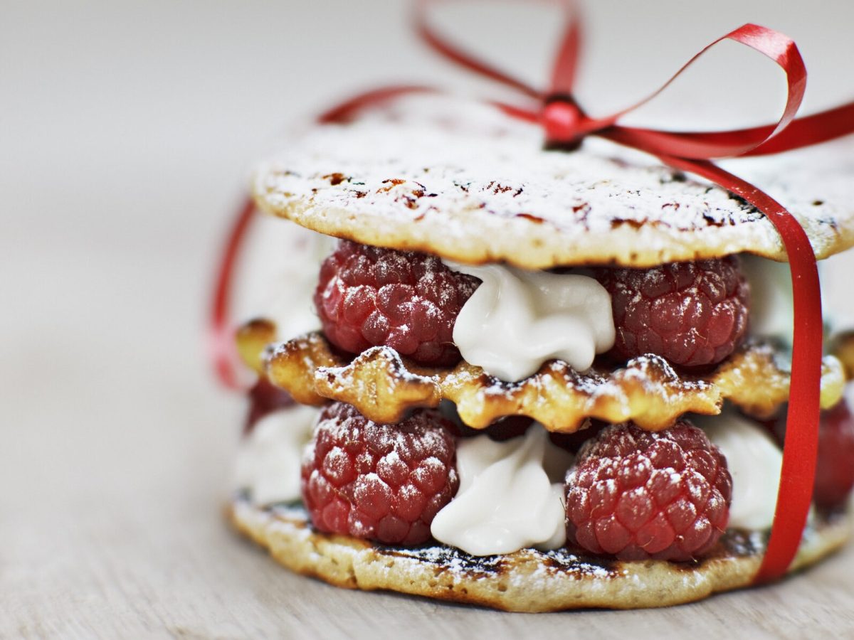 Ein Waffelturm aus belgischen Waffeln gefüllt mit Sahne und Himbeeren und mit einer roten Schleife verziert.