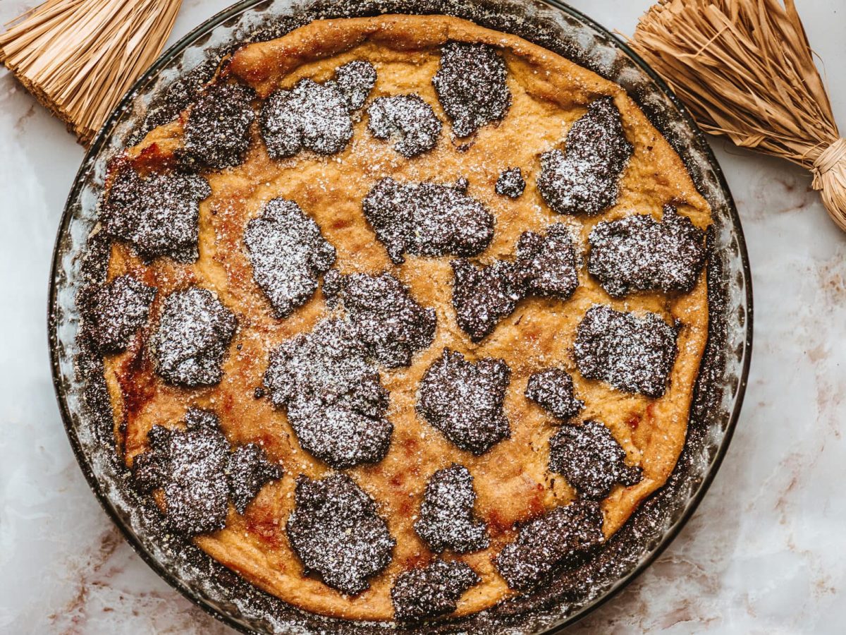 Ein Zupfkuchen mit Mohn und Marzipan in einer Kuchenform, von oben fotografiert. Drumherum etwas Deko aus Stroh und einige Muscheln.