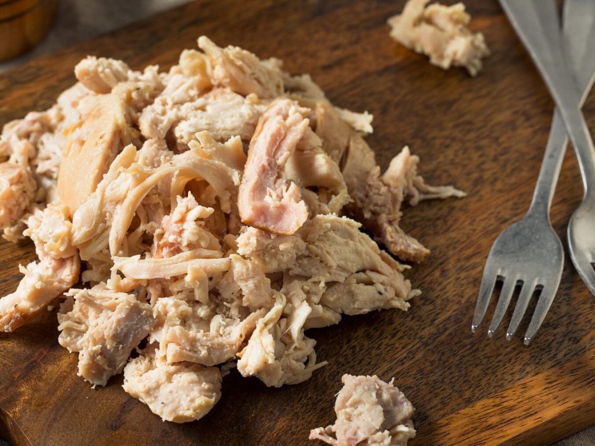 Eine Portion Pulled Chicken liegt auf einem braunen Holzbrett. Neben dem Pulled Chicken liegen zwei silberne Gabeln.