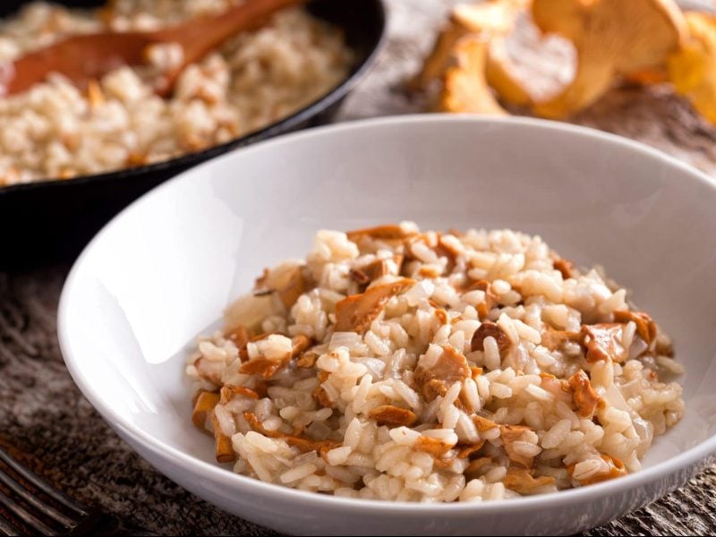 Auf einem rustikalem Tisch steht ein runder Teller, in dem ein Pfifferling-Risotto ist.