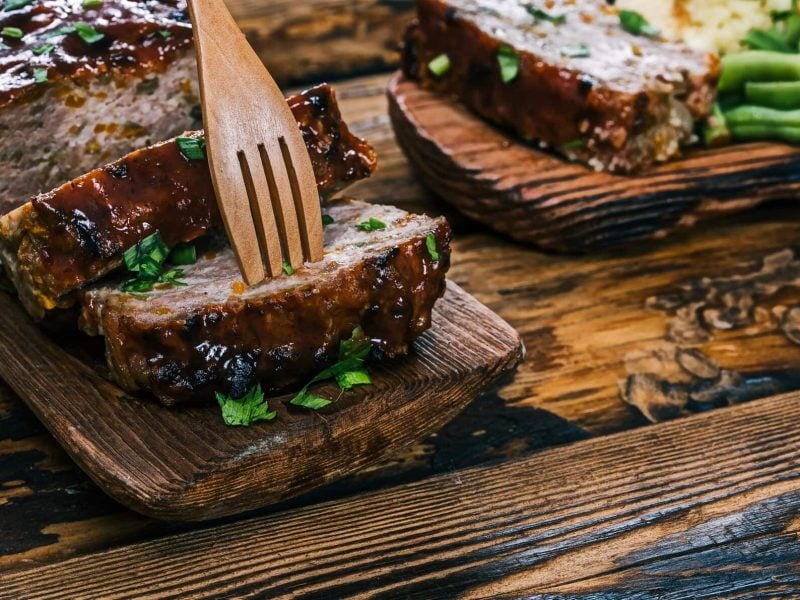 Auf zwei Holzbrettern liegen einige Scheiben Hackbraten mit Spinat und Feta, daneben grüne Bohnen.