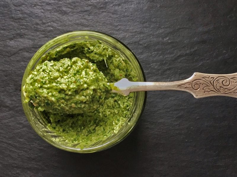 Ein Glas Möhrengrün Pesto mit einem Löffel vor dunklem Hintergrund, von oben.