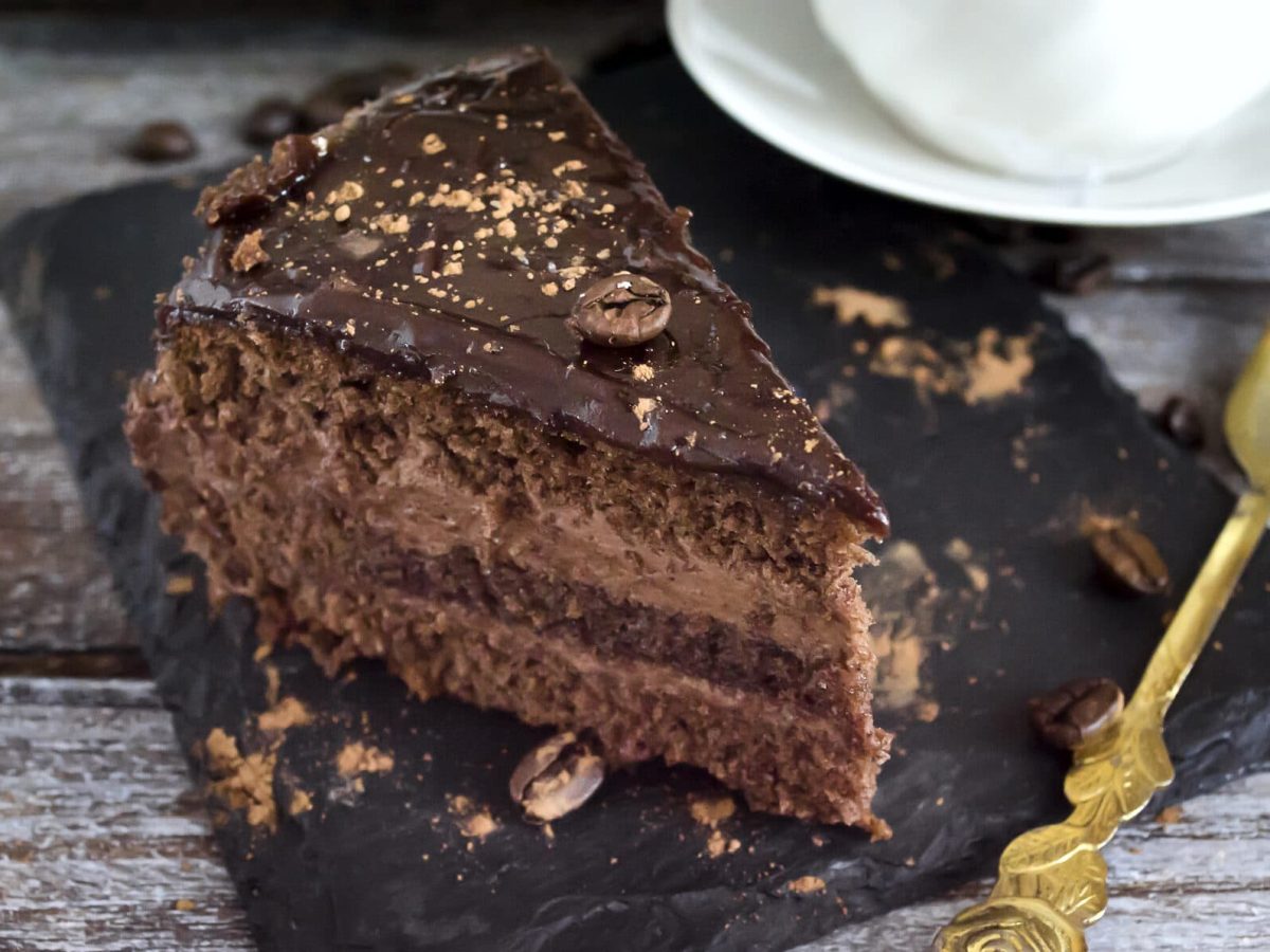 Ein Stück Mousse-au-Chocolat-Torte auf einer Schieferplatte, daneben liegt eine goldene Kuchengabel.