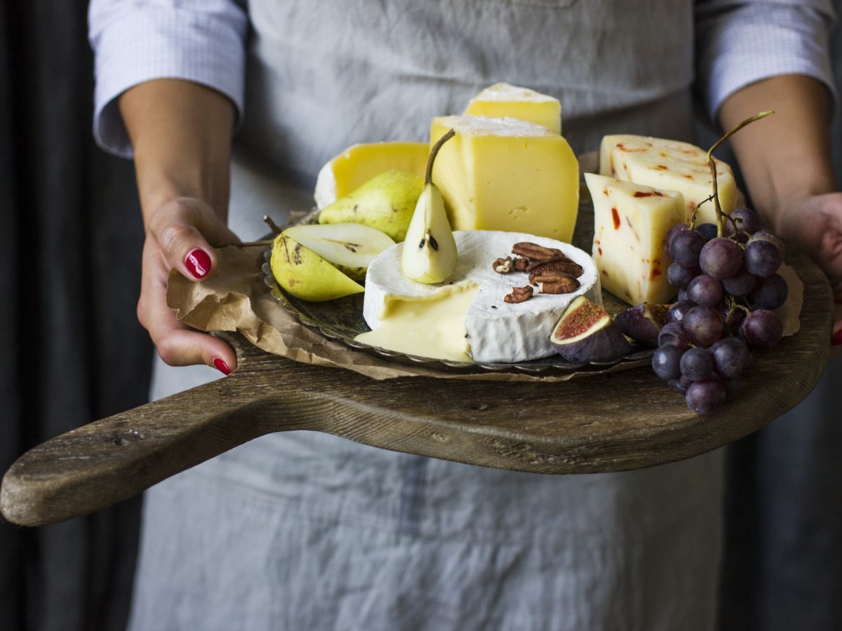 Was ist Lab? Eine Frau hält ein großes Holzbrett mit vielen verschiedenen Käse- und Obstsorten in den Händen.