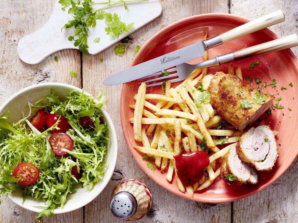 Die angeschnittene Cordon bleu-Roulade serviert auf einem Teller. Dazu gibt es einen grünen Salat mit Tomaten.