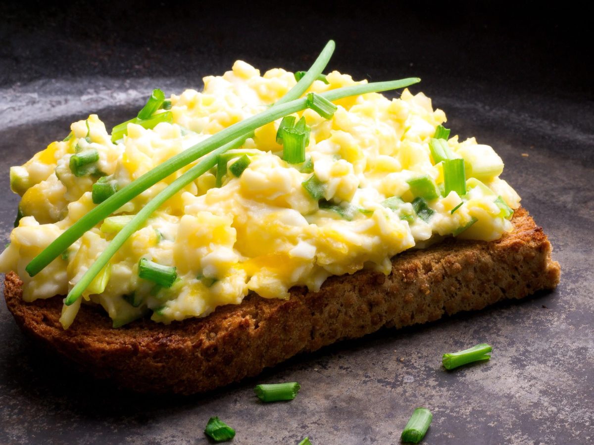 Brot belegt mit Eiersalat und Schnittlauch auf dunkler Arbeitsfläche.