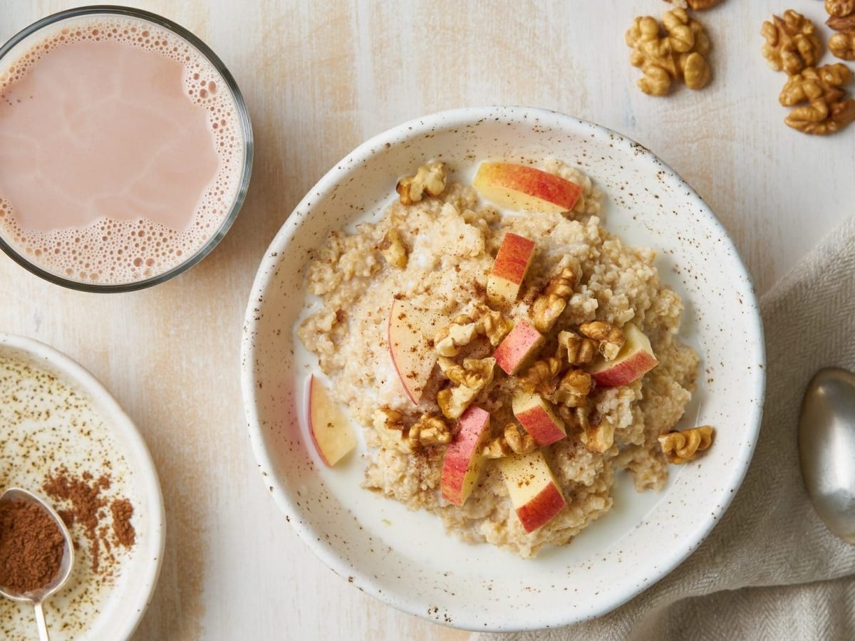 Der Haferbrei mit Nüssen und Apfel ist in einer weißen Müslischale angerichtet. Dazu gibt es eine Tasse Kakao.