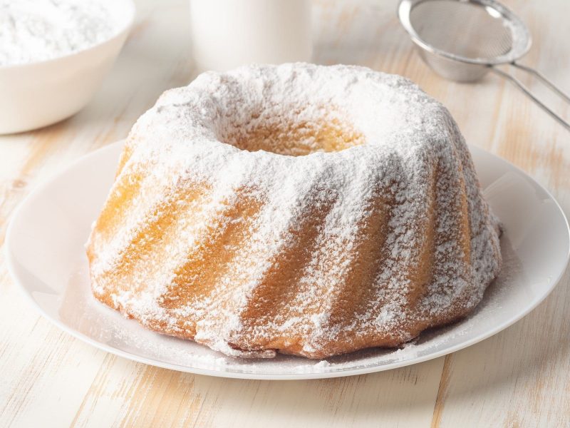 Saftiger Sandkuchen auf weißem Teller mit Puderzucker garniert.