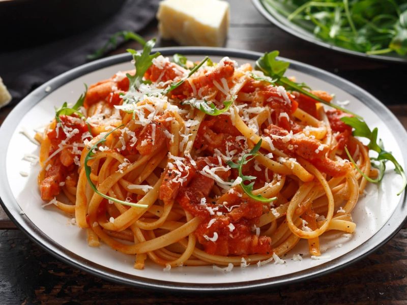 Auf einem großen Teller sind Spaghetti all amatriciana zu sehen. Es handelt sich um ein italienisches Traditionsgericht.