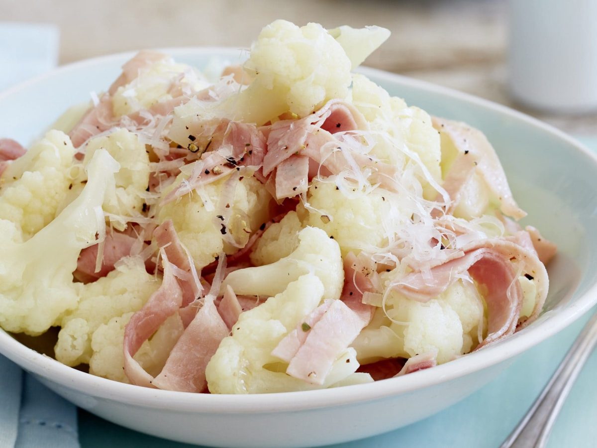 Feinste Blumenkohlröschen mit Schinkenstreifen und Parmesan in einem Teller angerichtet.